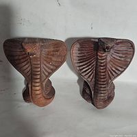 Front view of the pair of hand carved wooden cobra sculptures showing detailed flared hoods and textured scales.