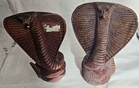 Pair of hand carved wood cobra sculptures shown from a top angled side view, highlighting their coiled bodies and spread hoods with detailed carvings