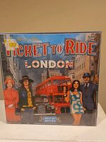 Front of the Ticket To Ride London board game box showing the logo, characters, and a London double-decker bus.