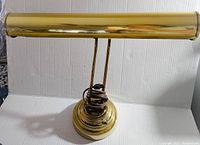 Front view of the vintage brass bankers lamp showing the long tubular shade and round base with wrapped power cord.