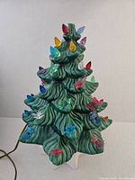 Front view of the green ceramic Christmas tree with multicolored light bulbs and decorative plastic bows and birds, showing the overall shape and design.