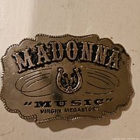 Front view of the metal belt buckle showing 'MADONNA' text, horseshoe emblem, and 'MUSIC' Virgin Megastore text.