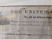 Close-up of the land deed showing the top of the document with printed text including 'THE UNITED STATES' and part of a vignette. Shows wear and creases.