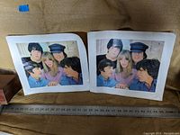 Two Beatles posters side by side on a carpet, showing the band members with a woman, size approximately 13x10 inches with visible wear and dust.