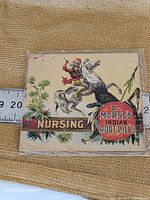 Close-up photo of vintage collectible paper ephemera featuring Dr. Morse's Indian Root Pills with colorful Indian on horse illustration, with ruler showing size around 4 inches wide.