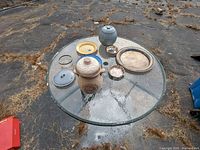 Full view of all items on round glass table outside on cracked ground.