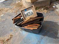 Large black bin filled with multiple framed photos and pictures, various sizes mostly wooden frames.