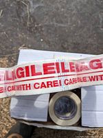 Close-up photo showing clear packing tape roll with red 'Fragile Handle with Care' print.