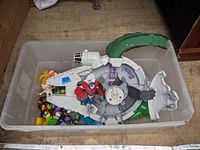 Plastic container holding Star Wars Millennium Falcon toy, Transformers figure, and other assorted toys.
