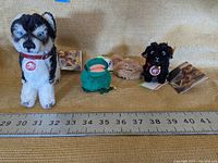 Four Steiff plush toys lined up on a surface with a measuring tape showing sizes around 6-7 inches for the dog plush.