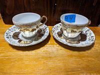 Two porcelain teacups with matching saucers, showing gold and floral pattern.