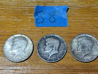 Three vintage Kennedy half dollar coins showing obverse profiles and dates 1964 and 1965.