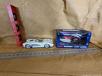 Photo showing white convertible toy car, Yamaha snowmobile model in box, with ruler indicating size.