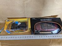 Two toy cars in their original boxes; left is V-DUB$ Meyers Manxter 2+2 with flame design in yellow packaging, right is red special edition model in black and red box