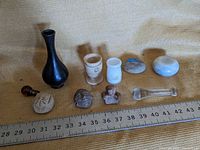 Photo of all 10 small trinkets arranged in a row on a fabric surface with ruler for scale, shows variety of small vases, cups, carved stones, and glass items