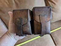 Leather pouch held in hand showing front view with two flap closures and straps