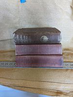 Side view showing three stacked vintage books with cloth covers and a ruler in the background to indicate size.