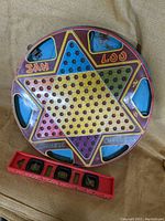 Full view of the vintage two-sided Chinese Checkers metal game board with six blue triangular pockets and a red plastic accessory for game pieces.