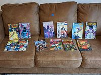 Photo shows a collection of comic books arranged on a brown leather couch. Visible titles include Thor, Wonder Woman, G.I. Joe, Teenage Mutant Ninja Turtles, Spawn, and Star Trek. Covers are colorful and the lot includes multiple individual issues and graphic novels.