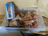 Overview of plastic storage bin filled with various vintage dolls and boxed doll