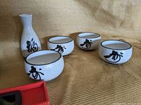 Close up of the four ceramic bowls and sake bottle showing detail of crackled glaze and black characters.