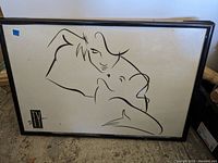 Framed print showing a minimalist black line drawing of two faces embracing, signed by Ty Wilson with 'TW' initials, metal frame with some dust and wear.