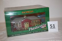 Front view of Bachmann Plasticville schoolhouse in original green box showing school building and playground equipment inside.