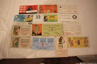 Photo showing all 13 advertising ink blotters arranged on white cloth, showcasing the variety of designs including birds, typewriters, tire advertisement, and illustrated women.