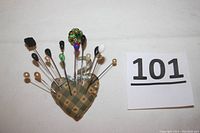 Hat pins inserted into a heart-shaped pin cushion laid on white background with lot number card visible.