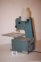 Front-left view showing saw frame, worktable, plastic water reservoir on top, and power cord.