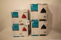 Photo showing four boxes with pendant lamps, two red and two black finishes, with model numbers 0394657 and 0394658 visible on packaging.