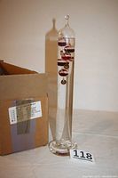 Full view of the Galileo thermometer with original box visible in background, showing height and overall condition.