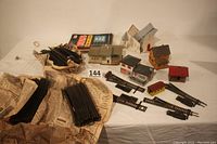 Photo showing brass HO scale curved track pieces wrapped in old newspaper dated 1978, a collection of HO scale buildings and softback books.