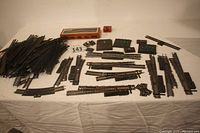 Wide view of lot showing many HO scale track pieces, switches, and several controllers arranged on white cloth.