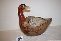 Full side view of the large hand-painted clay duck showing earthy tones, feather designs, and floral elements.