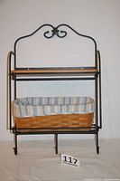 Black wrought iron rack with two shelves, basket on bottom, hooks on bottom, decorative scroll top