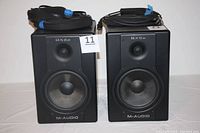 Pair of black M-Audio BX8a studio monitors with attached cables in used condition displayed together.