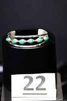 Open sterling silver bangle bracelet from Mexico displayed on a stand with six turquoise stones along a zigzag middle bar.