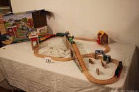 Full view of assembled wooden train set including tracks, bridge, Percy engine, extra engines, tunnel, and animal figures on 6-foot table.