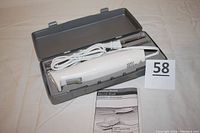 Hamilton Beach electric knife in gray carrying case with power cord coiled, two blades in plastic wrap, and bilingual instruction manual.