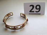 Gold filled cuff bracelet with rose gold flowers and leaves on an open band design, shown at an angled view