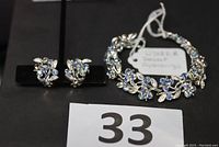 Photo of vintage Lisner bracelet with matching earrings displayed on black background, showing floral and leaf design with blue rhinestones.