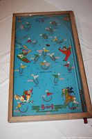 Full top-down view of the rectangular wooden framed Poosh-M-Up Big 5 pinball game board showing the blue playing surface decorated with colorful sport player illustrations, points markings, and metal ball targets. The red plunger is visible on the right side.
