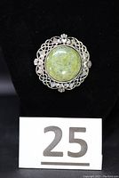Front view of the circular brooch featuring a green Connemara marble centerpiece and Celtic knot metalwork with hands and hearts motifs.