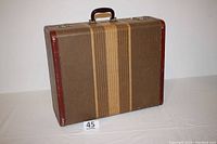 View of closed vintage suitcase front showing striped cloth exterior with brown leather corners and handle