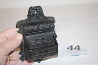 Close-up of vintage Wilton cast iron wall mount match holder showing size comparison holding it in hand.