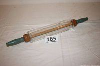 Full view of vintage clear glass rolling pin with wooden handles shown on white fabric background with lot number card 165