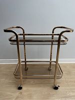 Front view of the rose gold bar cart showing front two caster wheels and two tinted glass shelves