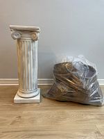 Photo showing full plaster column standing next to large clear bag of wicker baskets on floor.