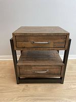 Front view of the rustic wooden end table showing two drawers with metal handles and metal frame sides.